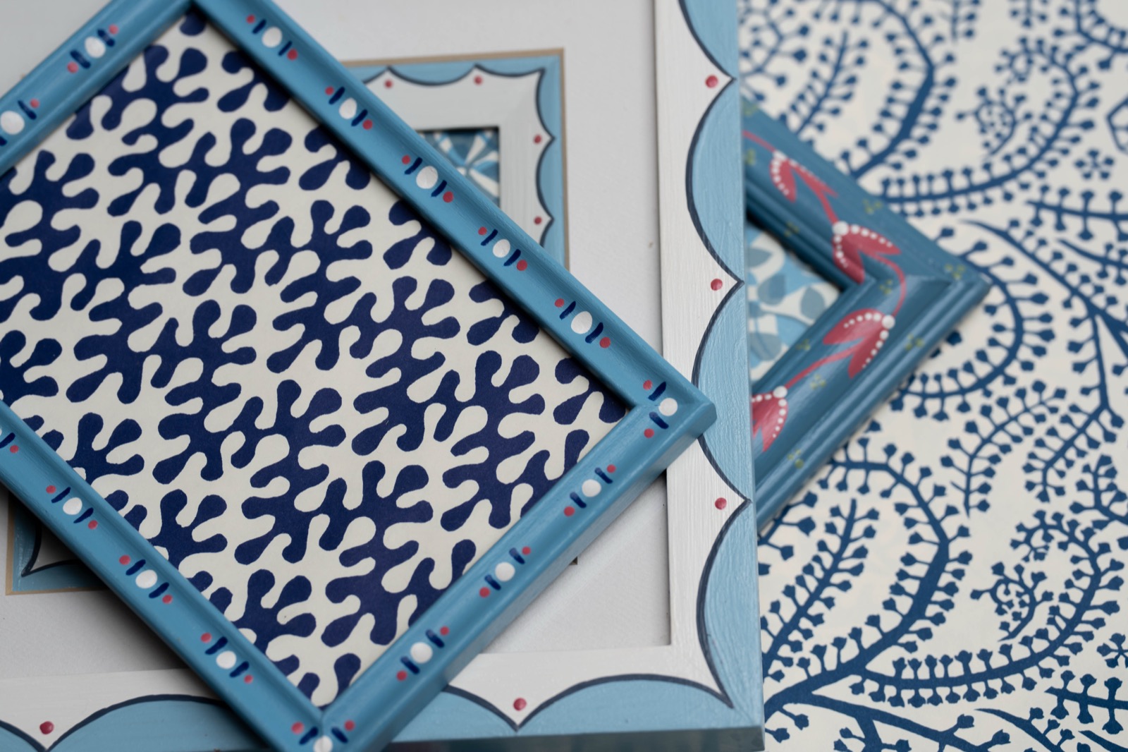 Blue hand painted frames with scalloped and dotted details, arranged over blue and white patterned paper.